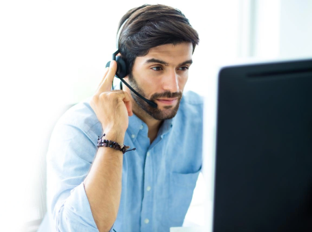 Man wearing a headset at a computer, assisting a caller.