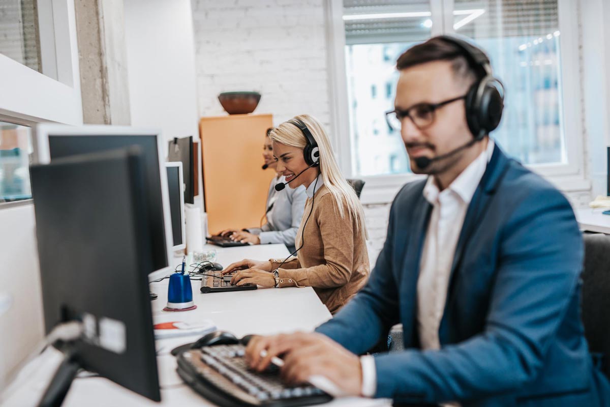 Customer service agents wearing headsets at their desks in a bright office.