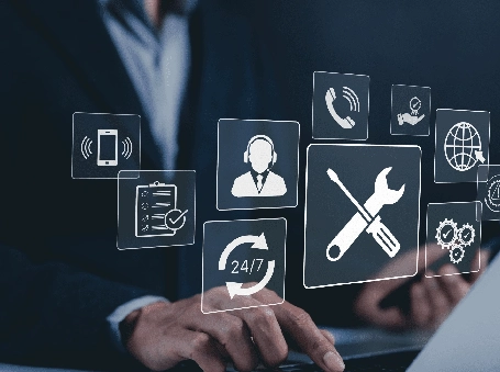 Professional in a suit typing on a laptop with translucent tech-support icons floating above, including a wrench & screwdriver to denote maintenance, 24/7 service, phone, and globe icons.