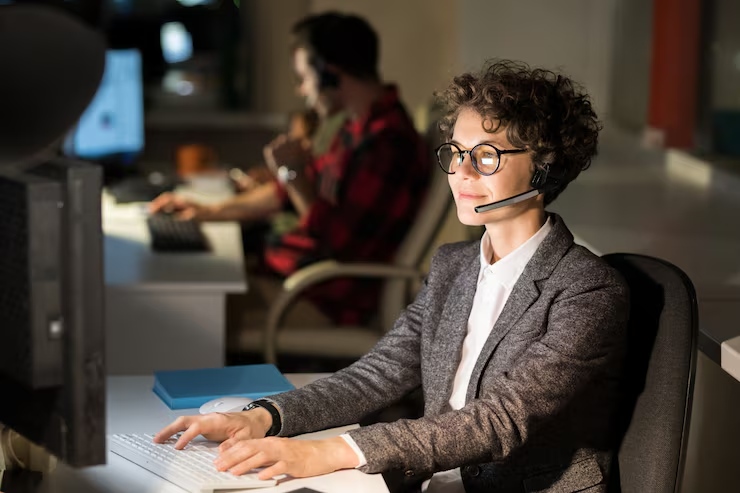 Customer support agent wearing a headset sits at a desk, typing on a keyboard in a call center.