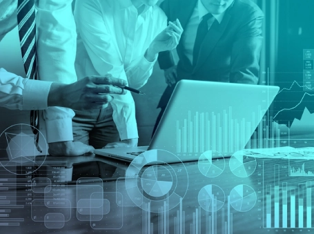 Team of professionals analyzes data on a laptop, pointing with a pen beside a chart-filled screen for a data analytics discussion