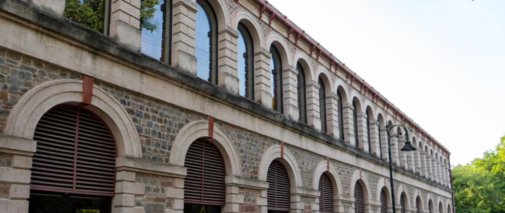 Long stone building with a repeating row of arched windows along the upper level, seen from the street.