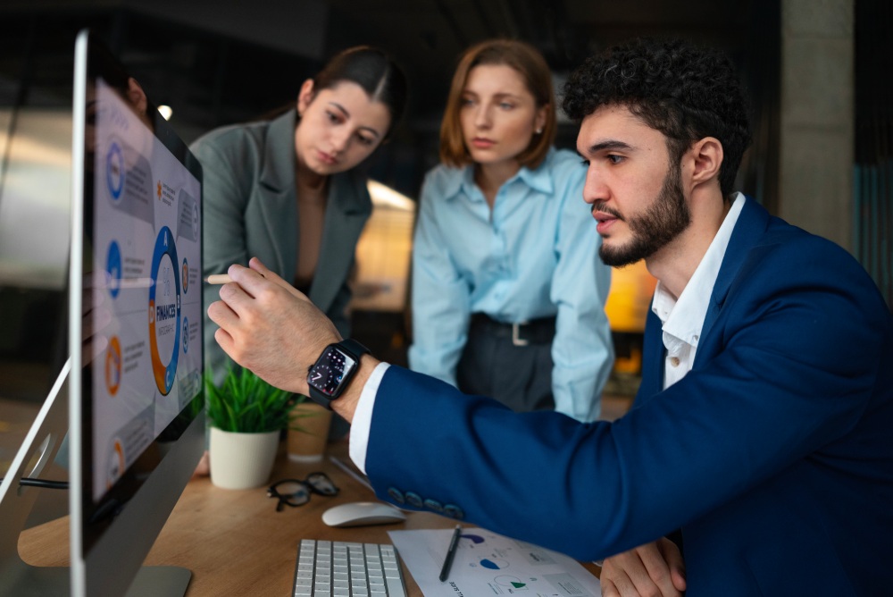 Group of professionals reviewing a data presentation on a desktop monitor, with one person pointing at the screen.